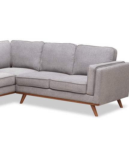 The Maddox RSF is a gray L-shaped sofa with wooden legs that combines mid-century modern style and contemporary design. It features plush cushions and clean lines, making it ideal for any modern living room.