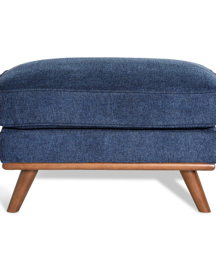 The Maddox Ottoman features textured blue upholstery and a rectangular cushion. Its mid-century design includes a wooden frame with four angled legs in a natural finish, making it an elegant addition to any living space.