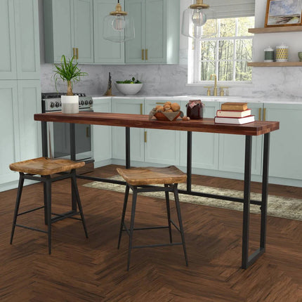 A modern kitchen features light green cabinets, a marble backsplash, a wood island with eco-friendly furniture, two rustic stools, books, and a plant centerpiece on herringbone wood flooring. Pendant lights and a window add natural light. The Rosewood Console enriches the space.